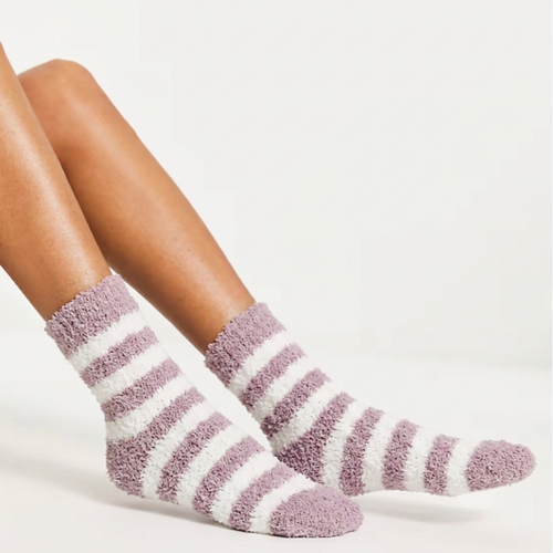 Women's bed socks in lavender and white plush, featuring fuzzy striped bands. Worn on legs in a relaxed cozy pose.