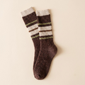 A pair of ribbed crew socks in dark brown with cream and olive green stripes, laid flat on a light beige background.