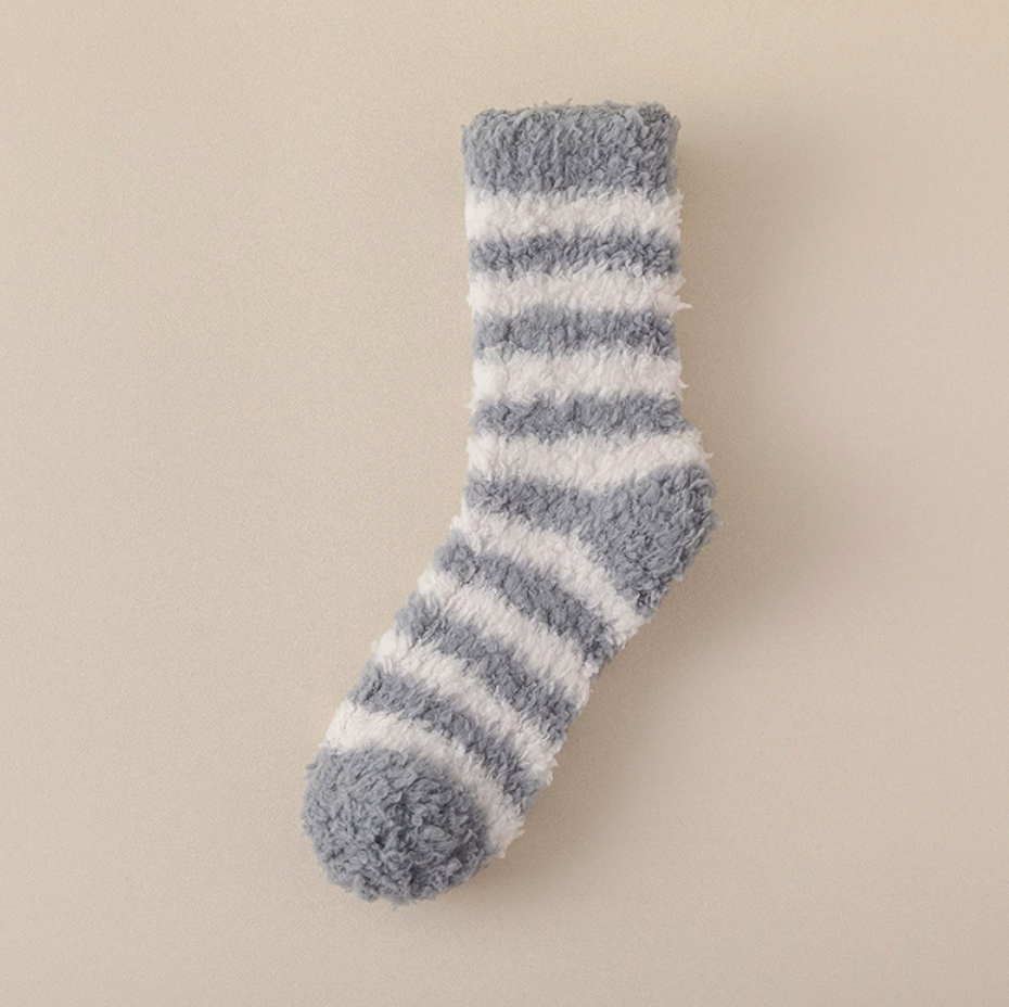 Best sleeping socks for cold feet in grey and white fuzzy fleece, featuring soft striped bands. Displayed as a single flat-lay against a beige surface.