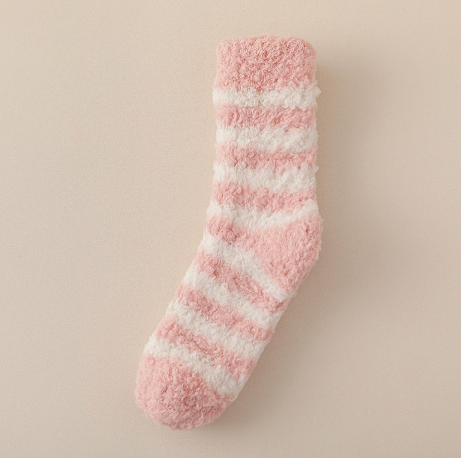 Best sleeping socks for cold feet in pink and white plush knit, featuring fuzzy horizontal stripes. Shown as a single angled flat-lay on a warm neutral backdrop.