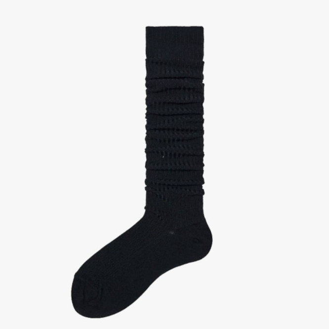 Black slouch socks in soft knit, featuring a bunched slouchy leg. Worn on one foot in a relaxed style.
