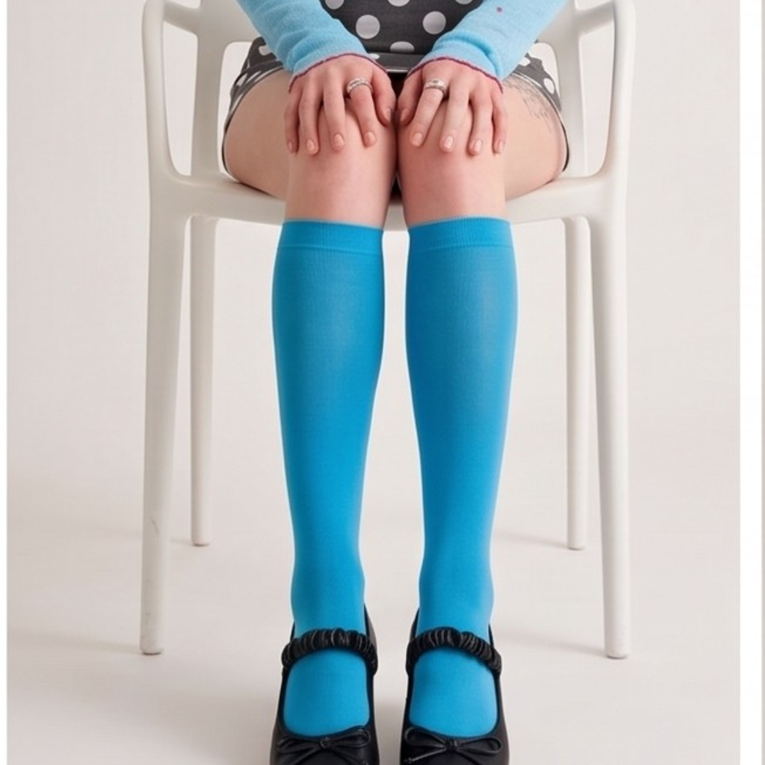 Blue fashion knee socks in vivid blue knit, featuring a lightweight sheer texture. Shown seated on a white chair.
