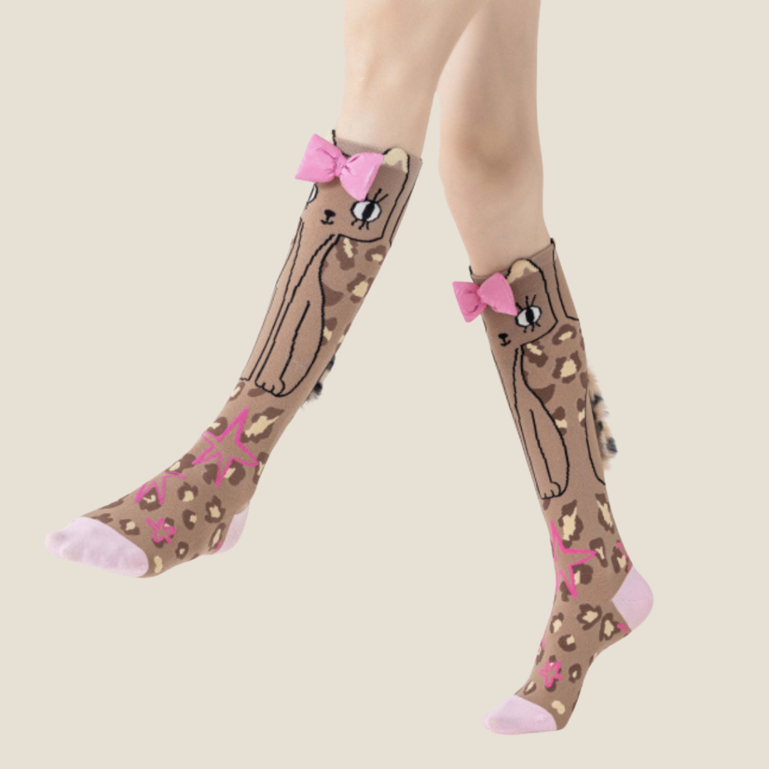 Cat knee socks in brown with a cute cat design, featuring a pink bow. Worn on legs in a playful pose.
