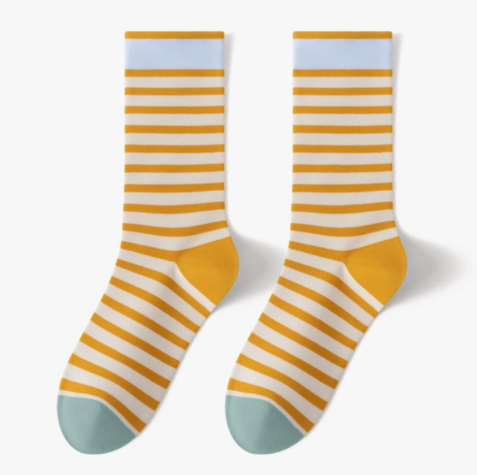 Comfortable crew socks in mustard and white stripes with a tan toe, featuring a ribbed cuff. Shown as a flat-lay pair on a neutral backdrop.