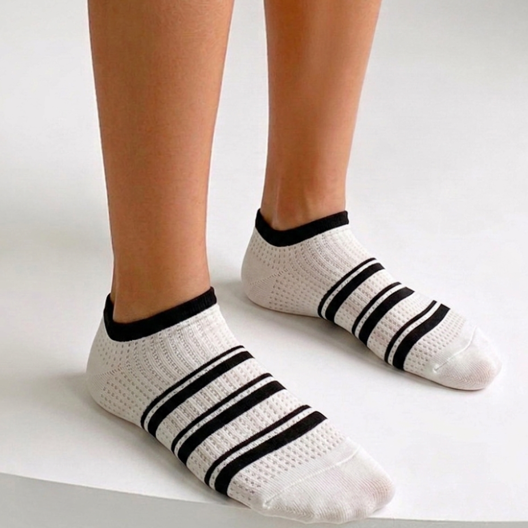 Comfy ankle socks in cream with black stripe accents, featuring a soft cushioned knit. Worn on feet in a bright setting.