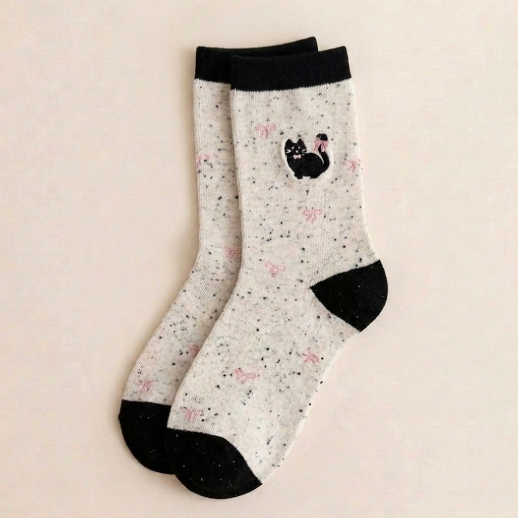 Cotton cat socks in the Bowknot style, cream speckled knit with an embroidered black cat and red bow, flat-lay pair.