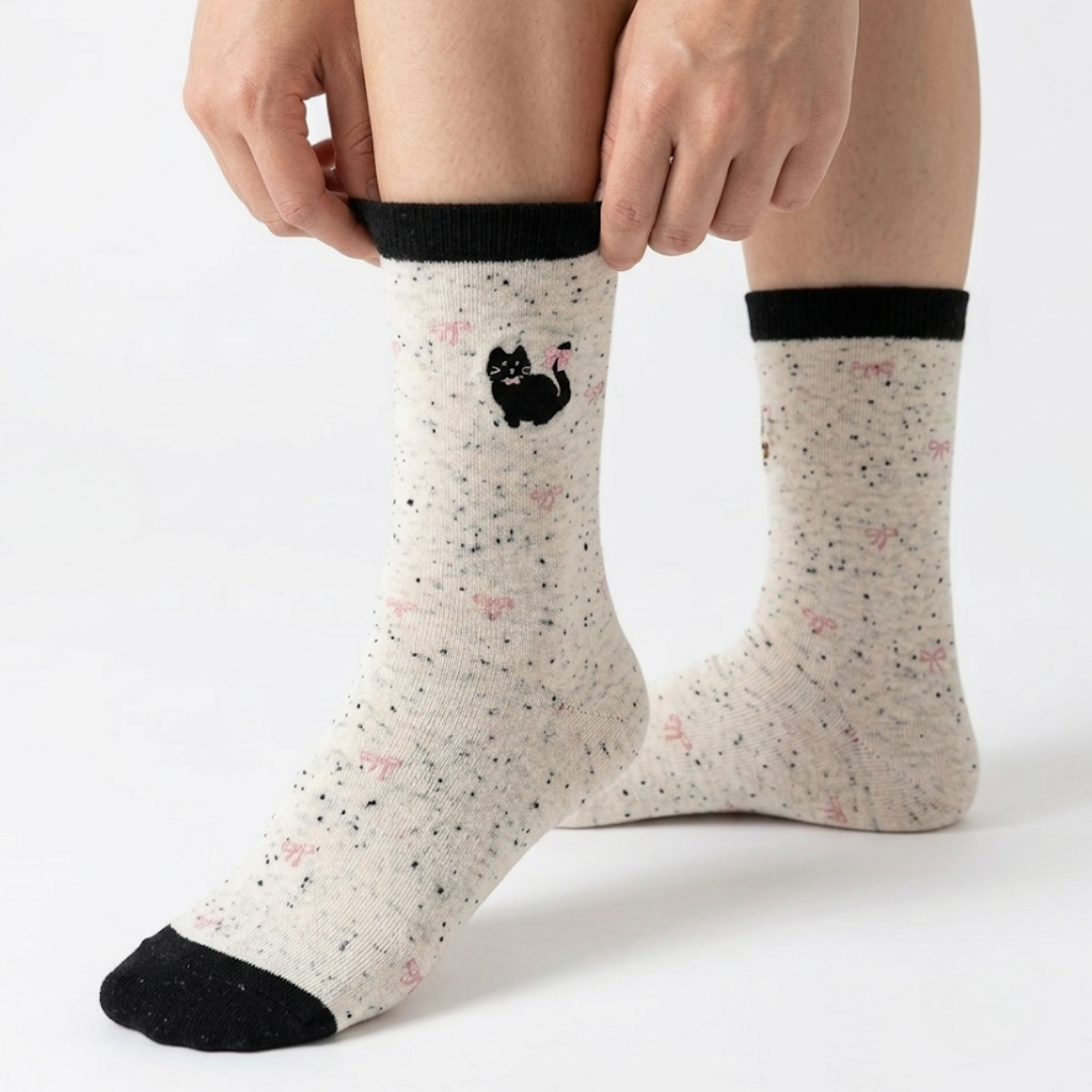 Cotton cat socks in cream speckled knit with a small black cat and black cuff, worn on the feet, side view.