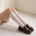 Cotton knee socks for women in cream cable knit, featuring a textured leg. Worn with brown loafers in a seated pose.