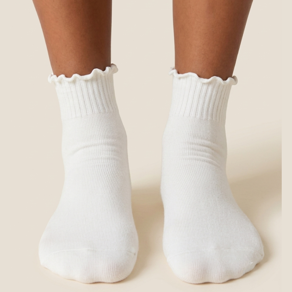 Cotton ruffle socks in white with a lettuce-ruffle cuff, worn on the feet, front view.