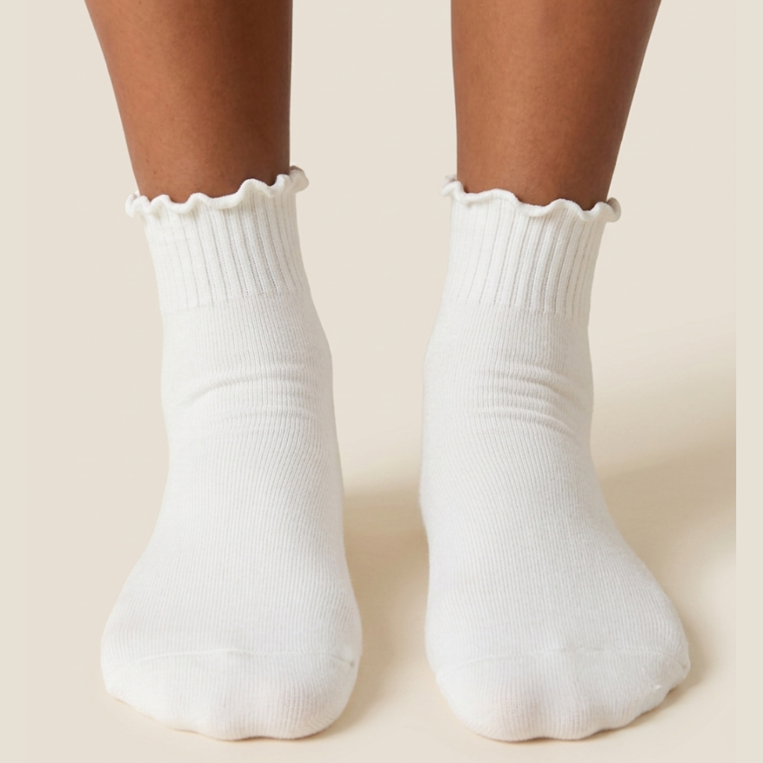 Cotton ruffle socks in white with a lettuce-ruffle cuff, worn on the feet, front view.