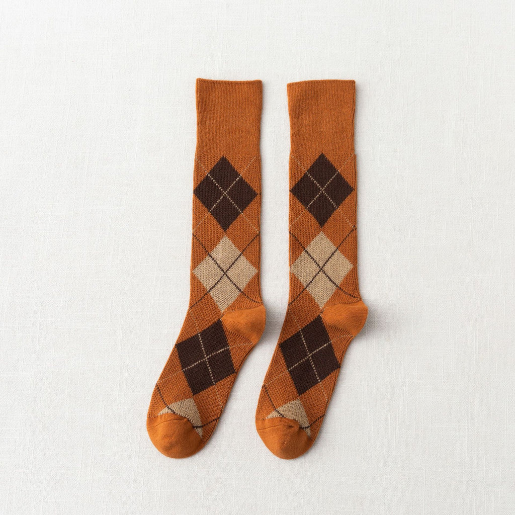 Cotton socks for loafers in orange and cream argyle pattern, shown as a flat-lay pair on a linen background.
