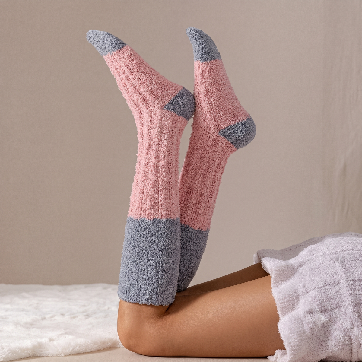 Cozy knee high socks in pink plush knit, featuring grey colorblock cuffs and heels. Worn on legs raised in a relaxed pose.