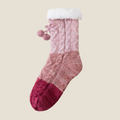 Crochet slipper socks in pink, featuring pom-pom accents and a knit cuff. Shown as a single flat-lay on a neutral backdrop.