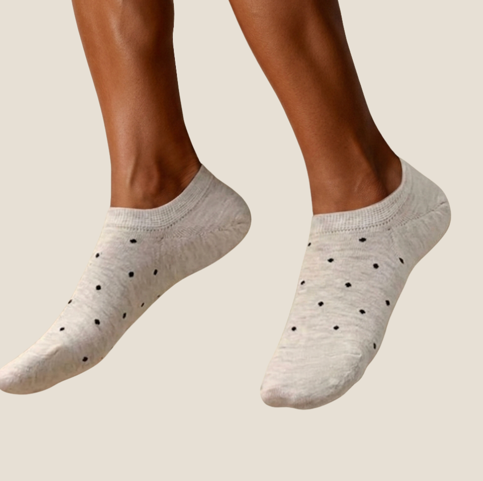 Cute ankle socks in oatmeal with black polka dots, featuring a low-cut design. Worn on feet in a warm setting.