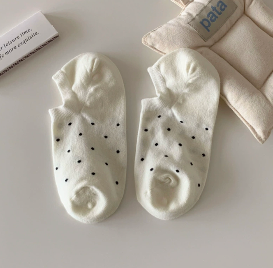 Cute ankle socks in white with black polka dots, featuring a bow and frill cuff. Shown as a flat-lay pair on a soft surface.