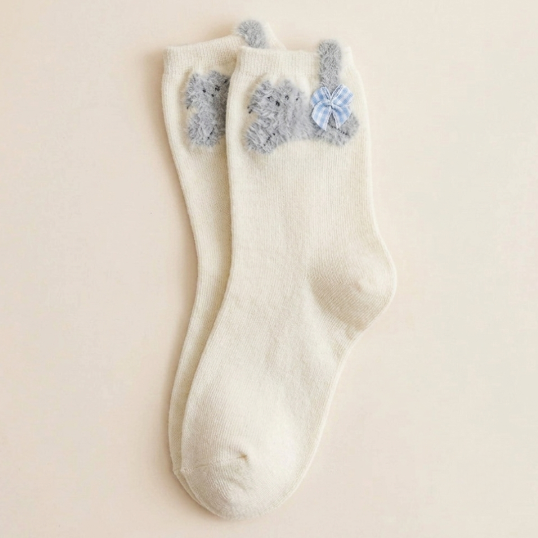 Cute cat socks in ivory white with fuzzy cat ears and pompoms, single sock laid flat.