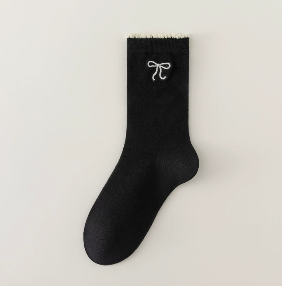 Cute crew socks in black knit, featuring a white bow embroidery. Shown as a single flat-lay on a neutral backdrop.