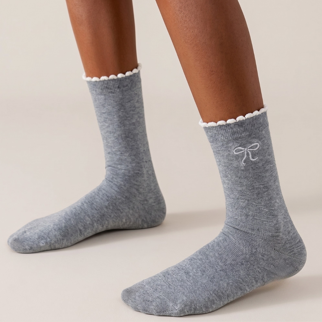 Cute crew socks in grey knit, featuring a ruffle cuff and bow accent. Worn on the feet in a sweet look.