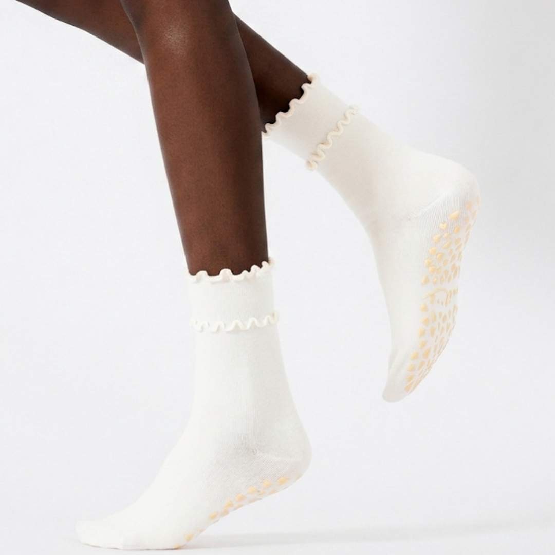 Cute grip socks in ivory with a scalloped trim and dotted non-slip sole, shown on a foot.