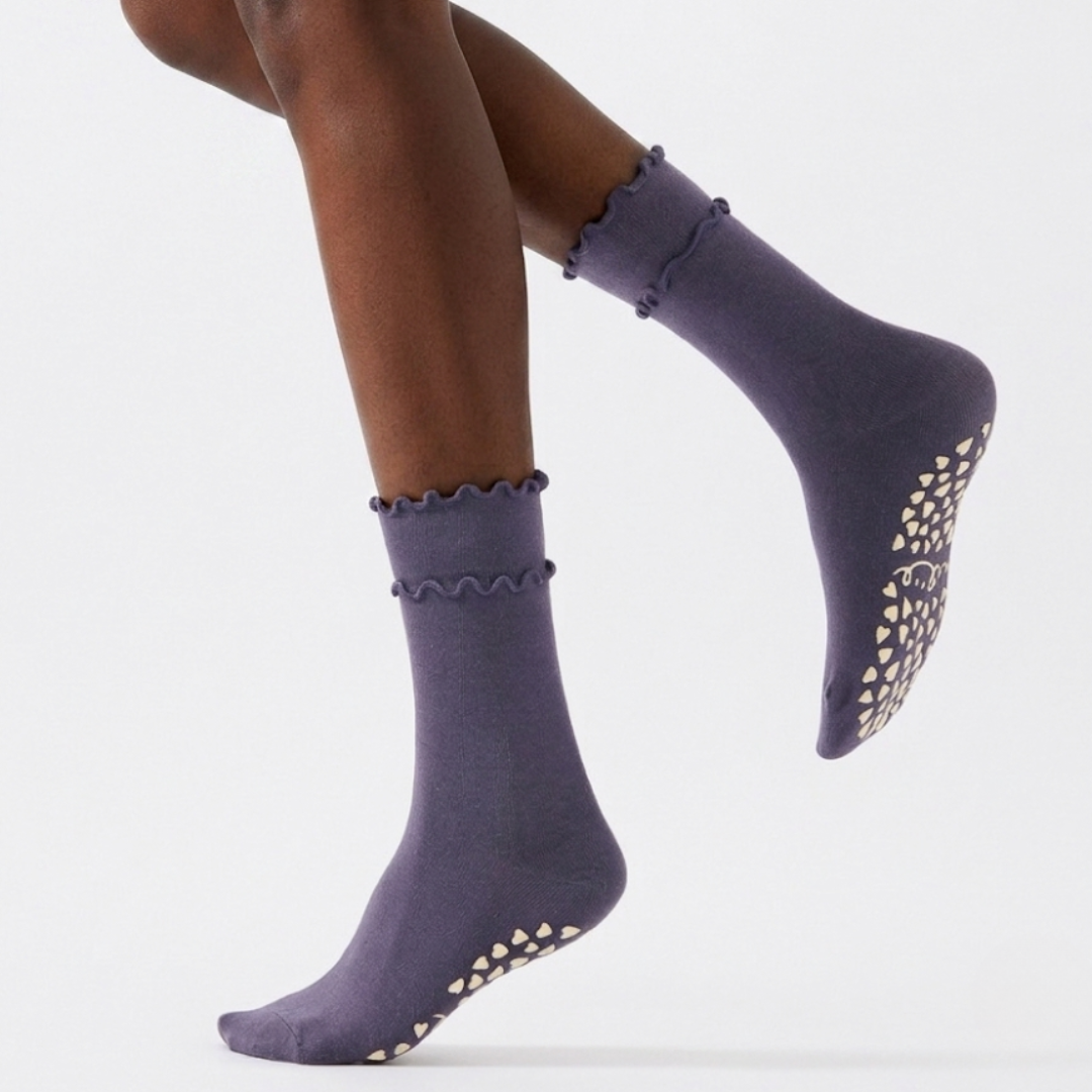 Cute grip socks in purple with a ruffle cuff, worn on the legs with the grip sole facing out.