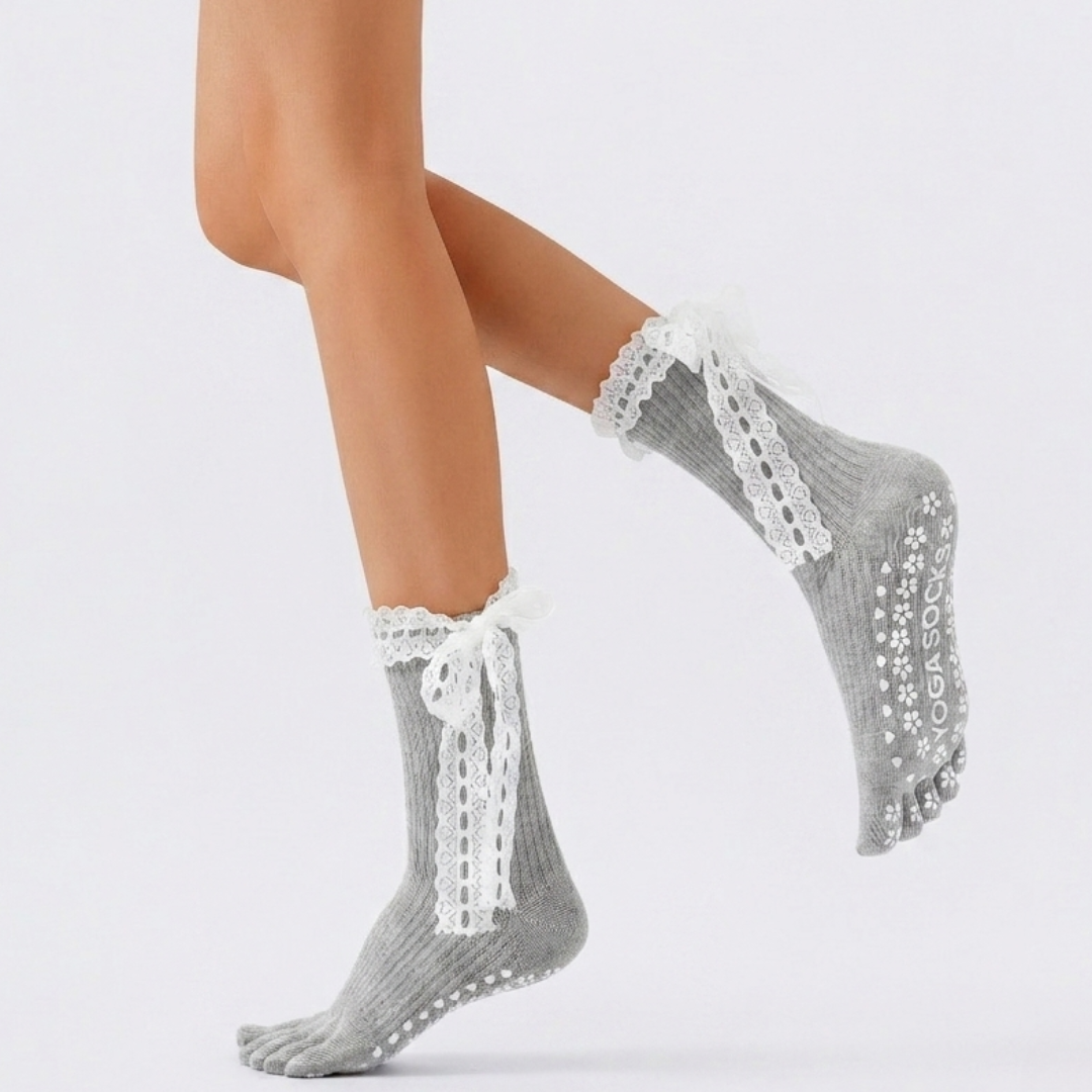 Cute pilates grip socks in gray split-toe knit with a lace tie bow and silicone grip sole, worn on the feet.