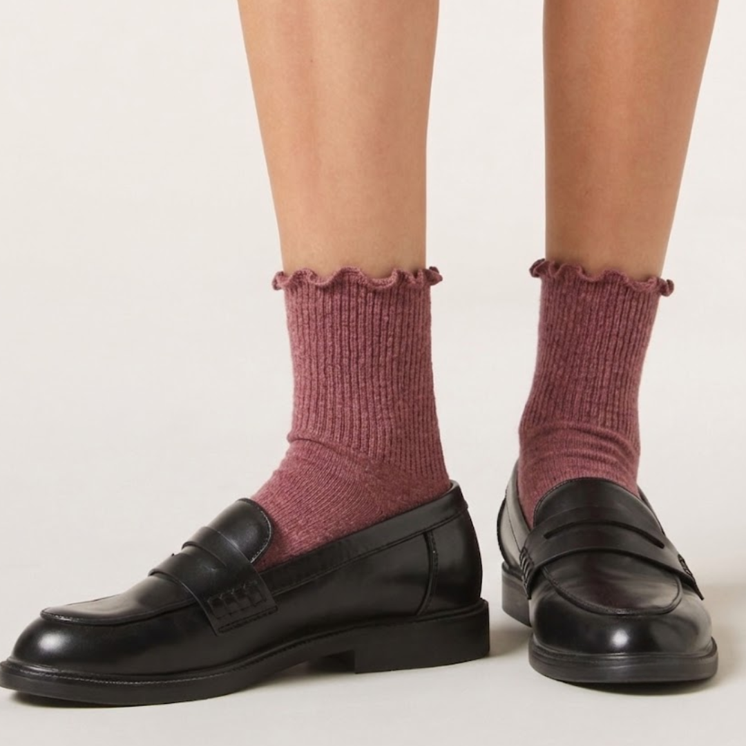Cute socks for loafers in berry red with a ruffle lettuce-edge trim, styled on the legs with black loafers, side view.