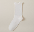 Cute socks for loafers in white with a ruffle trim, a single sock shown upright against a soft neutral backdrop.