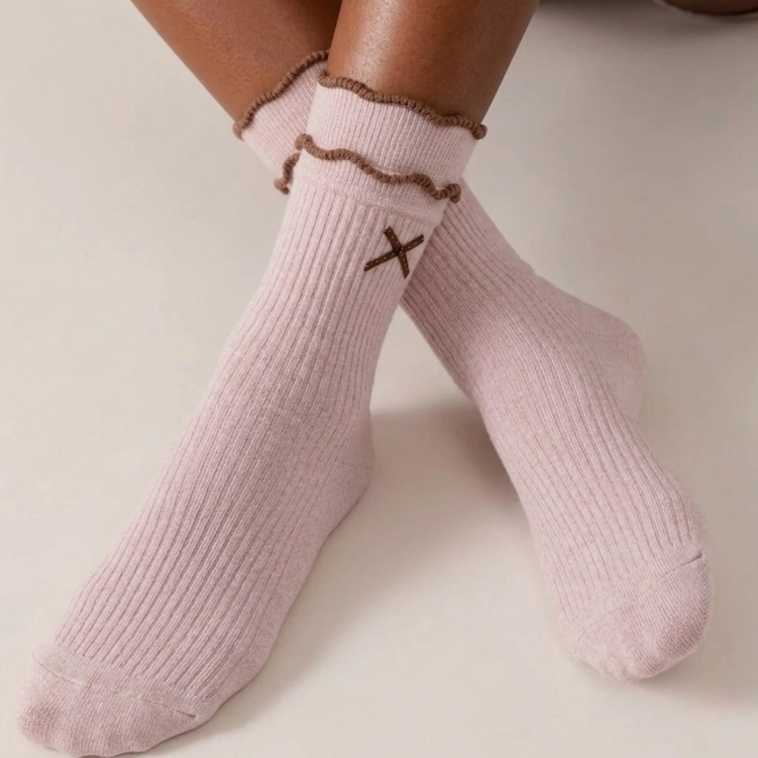Pink cute socks in ribbed cotton with a ruffle cuff and bow detail, worn on the feet, front view.
