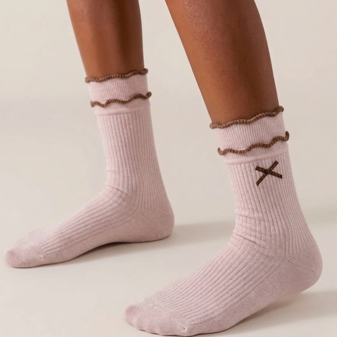 Pink cute socks with a ruffle cuff and embroidered bow, shown on the feet, side view.