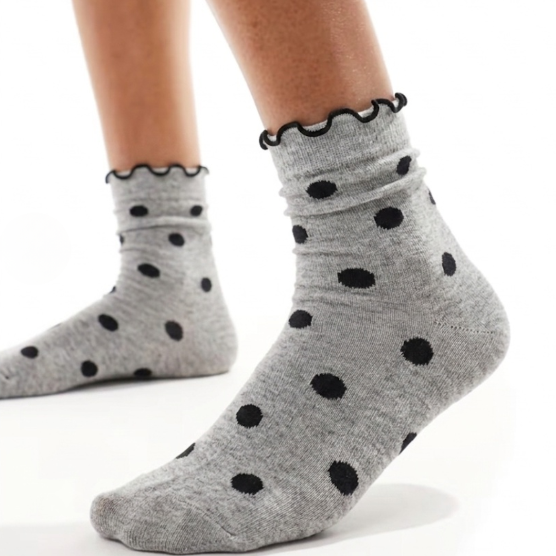Cute socks with ruffles in gray with black polka dots and a ruffle cuff, worn on the feet, side view.