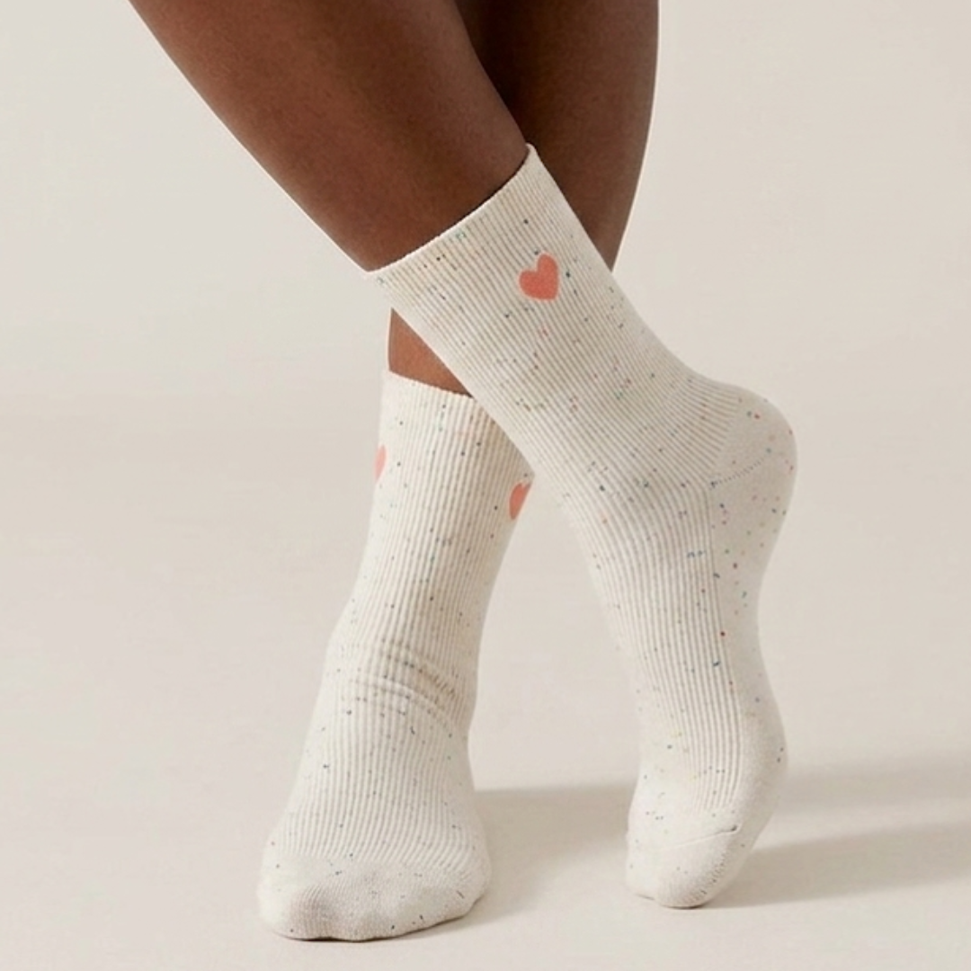 Embroidered crew socks in cream knit, featuring a small red heart motif. Worn on the feet in a soft setting.