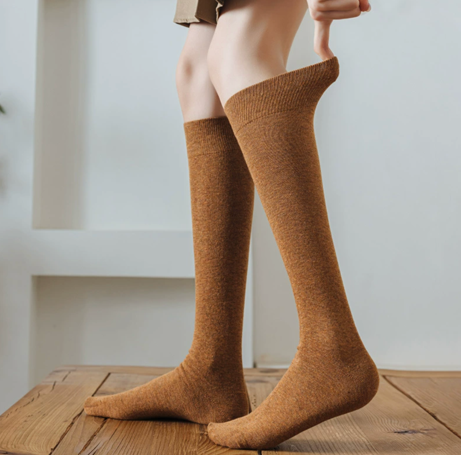 Female knee socks in camel tan ribbed knit, featuring a stretchy leg. Shown being pulled up on the leg.
