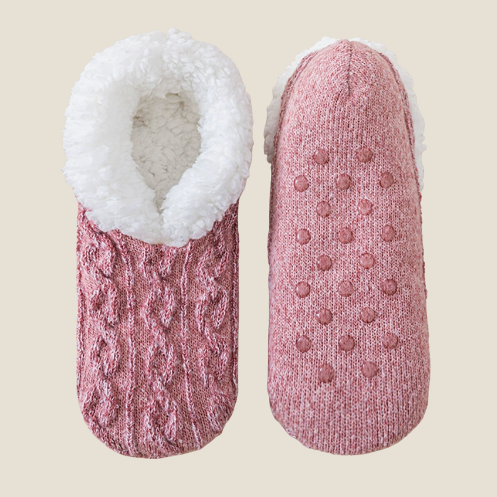 Fleece lined slipper socks in mauve cable knit, featuring a sherpa cuff and non-slip sole. Shown as a flat-lay pair on a neutral backdrop.