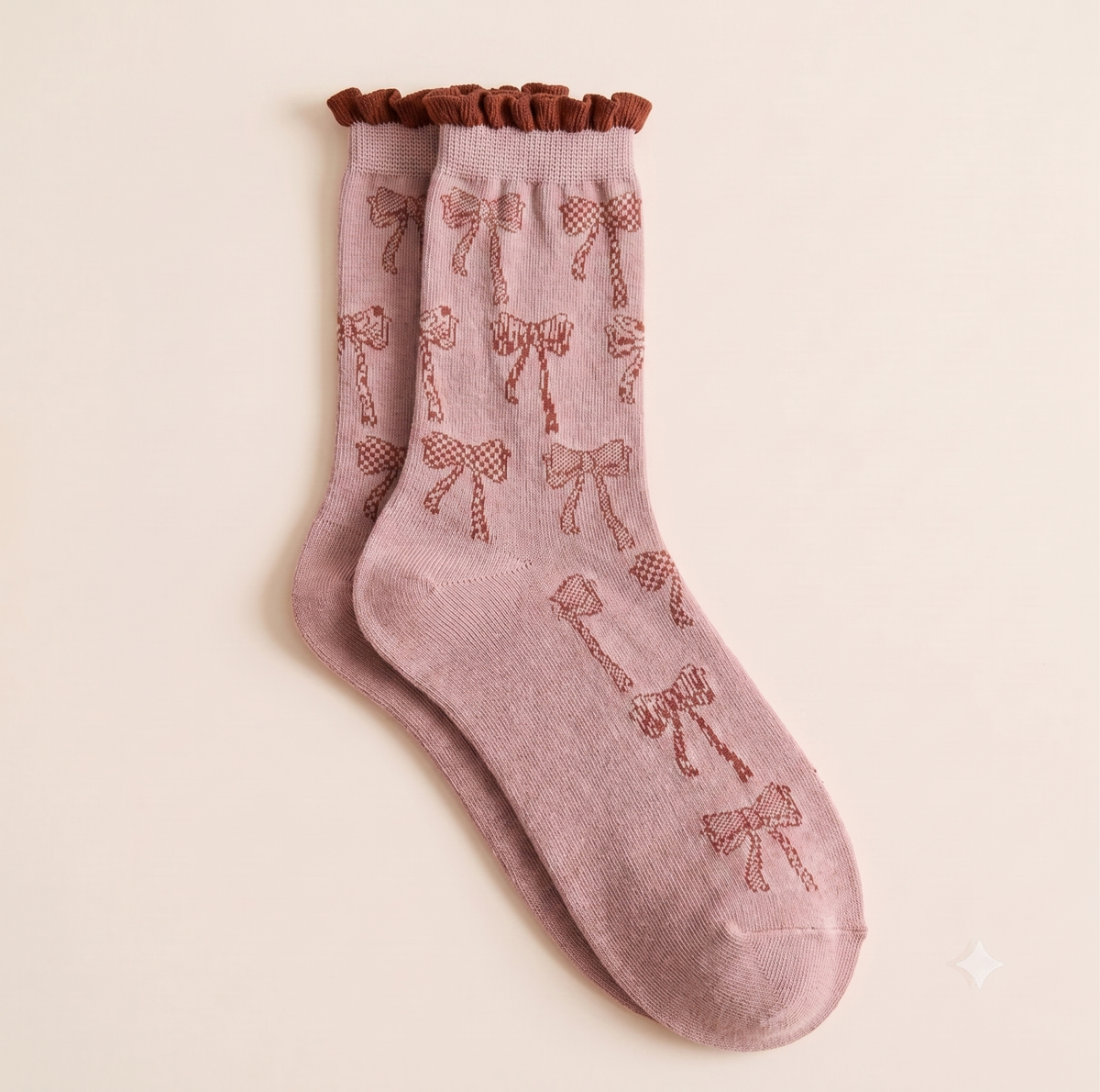 Girls' boot socks in soft pink, featuring a bow motif and frilled cuff. Shown as a flat-lay pair on a light surface.