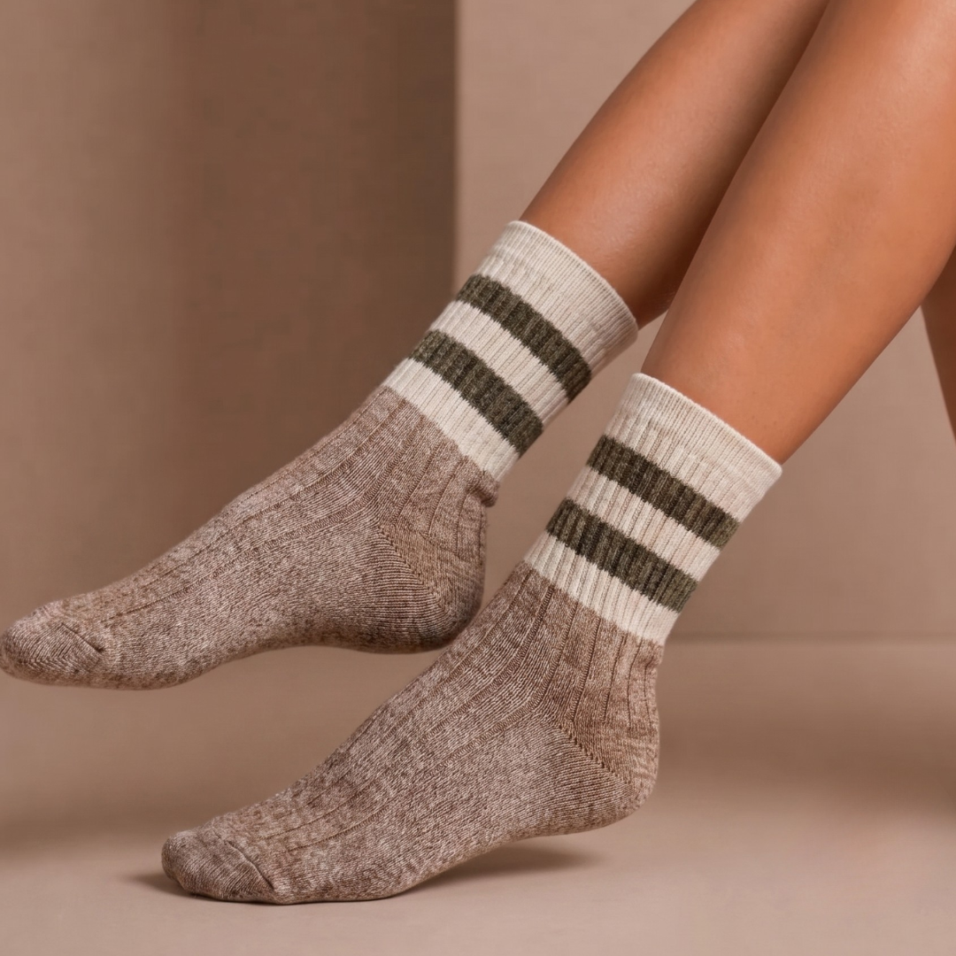 Half crew socks in oatmeal marled knit, featuring black varsity stripes. Worn on the feet in a relaxed pose.
