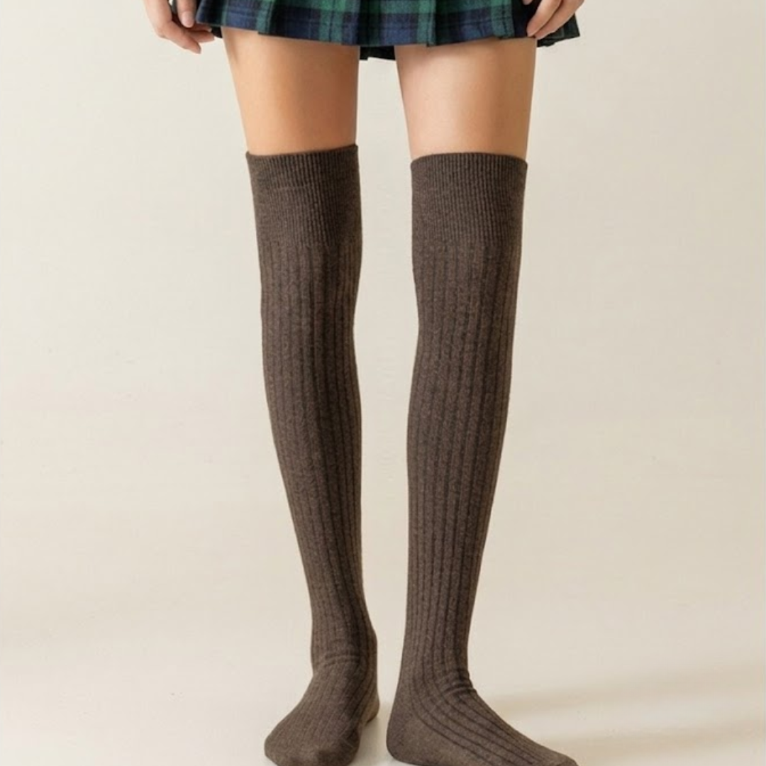 Knee high boot socks in taupe brown, featuring a ribbed knee-high length. Worn on legs styled with a plaid skirt.