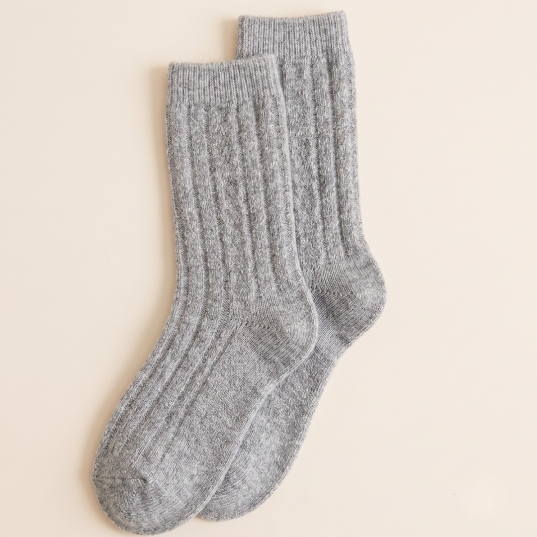 Knit boot socks in grey marled wool, featuring a cozy cable-knit texture. Displayed flat as a pair on a light backdrop.