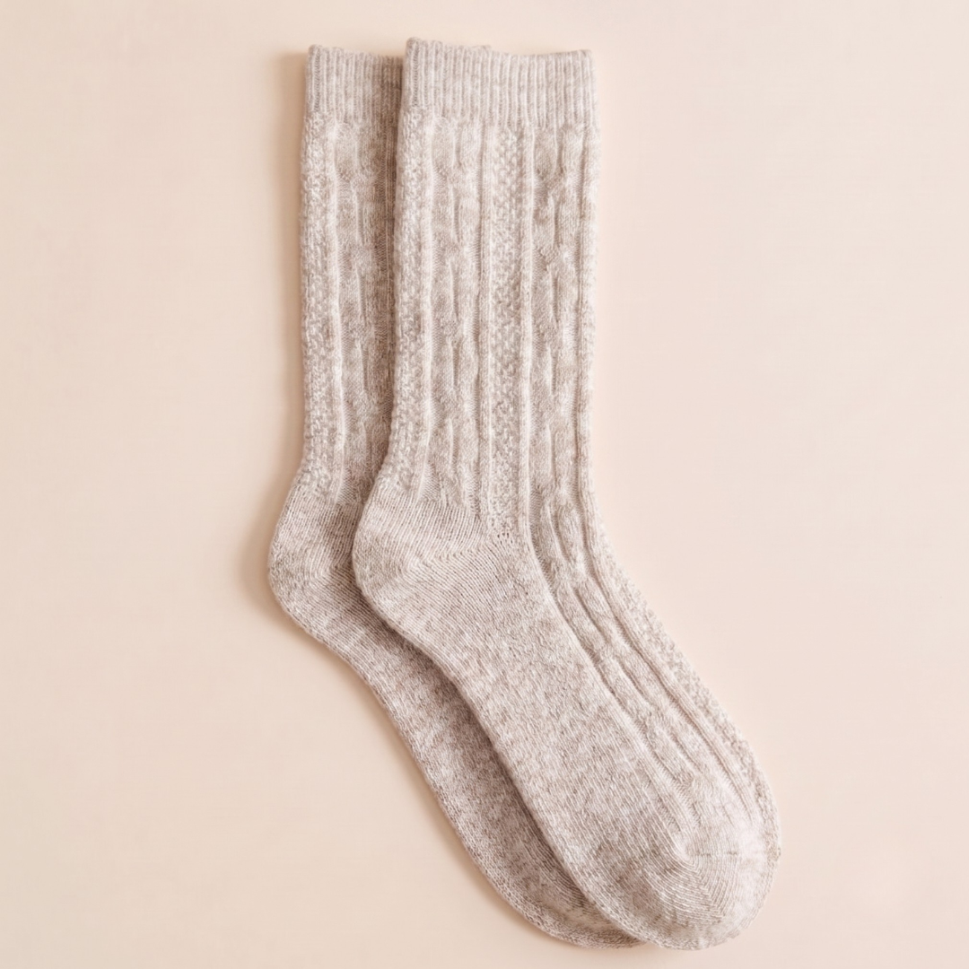 Knit boot socks in oatmeal marled wool, featuring a chunky cable-knit body. Shown as a single flat-lay on a warm surface.