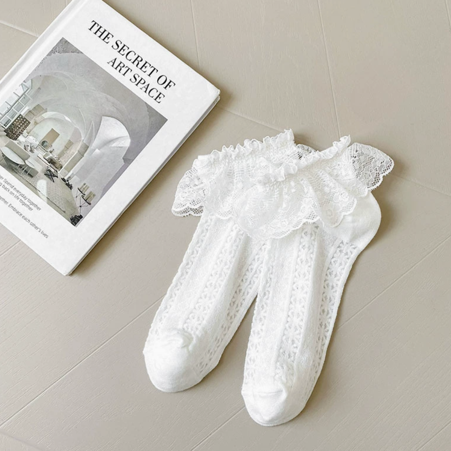 Lace ankle socks in white, featuring a delicate lace ruffle cuff. Displayed flat as a pair on a styled surface.