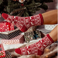 Luxury Christmas socks in red reindeer Fair Isle knit, held near a decorated tree with wrapped gifts.
