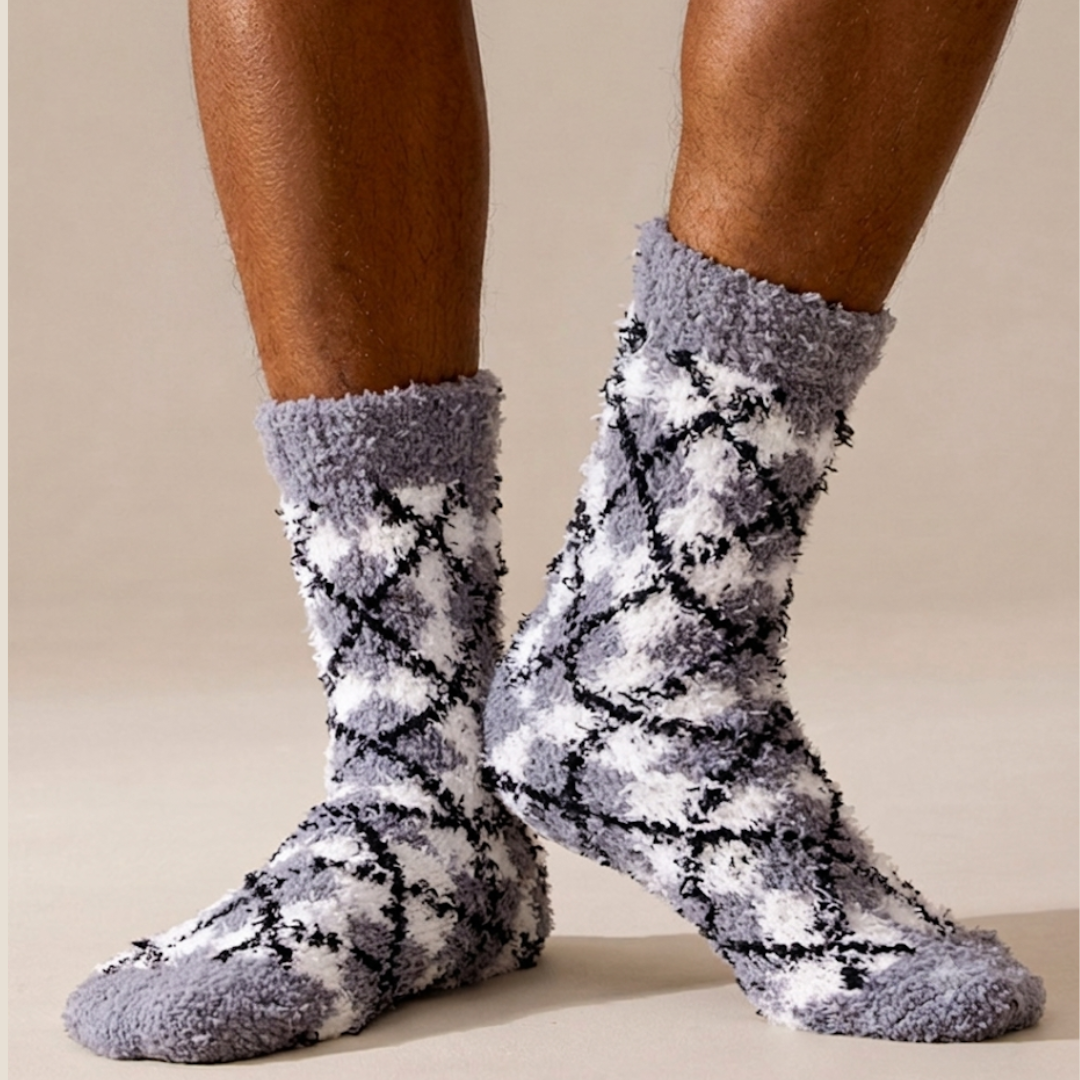 Men's bed socks in navy fuzzy knit, featuring a white argyle diamond pattern. Worn on feet and legs in a cozy indoor setting.