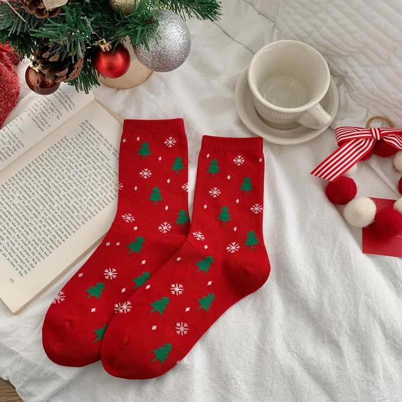 Men's Christmas socks in red with a green Christmas-tree pattern, flat-lay pair with holiday decorations.