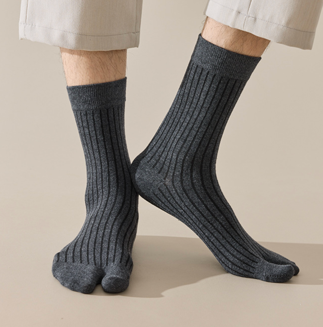 Men's tabi socks in charcoal grey, featuring a split-toe ribbed knit. Worn on feet with rolled trousers.