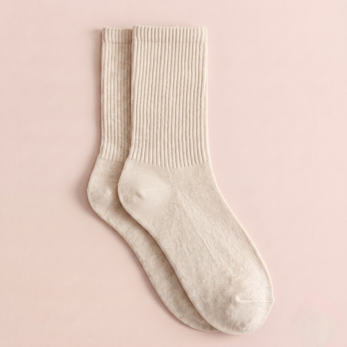Merino wool dress socks in ivory ribbed wool, featuring a soft cuff. Displayed flat as a pair on a pink backdrop.