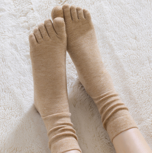 Merino wool toe socks in beige knit, featuring soft five-toe styling. Worn on crossed feet in a cozy setting.