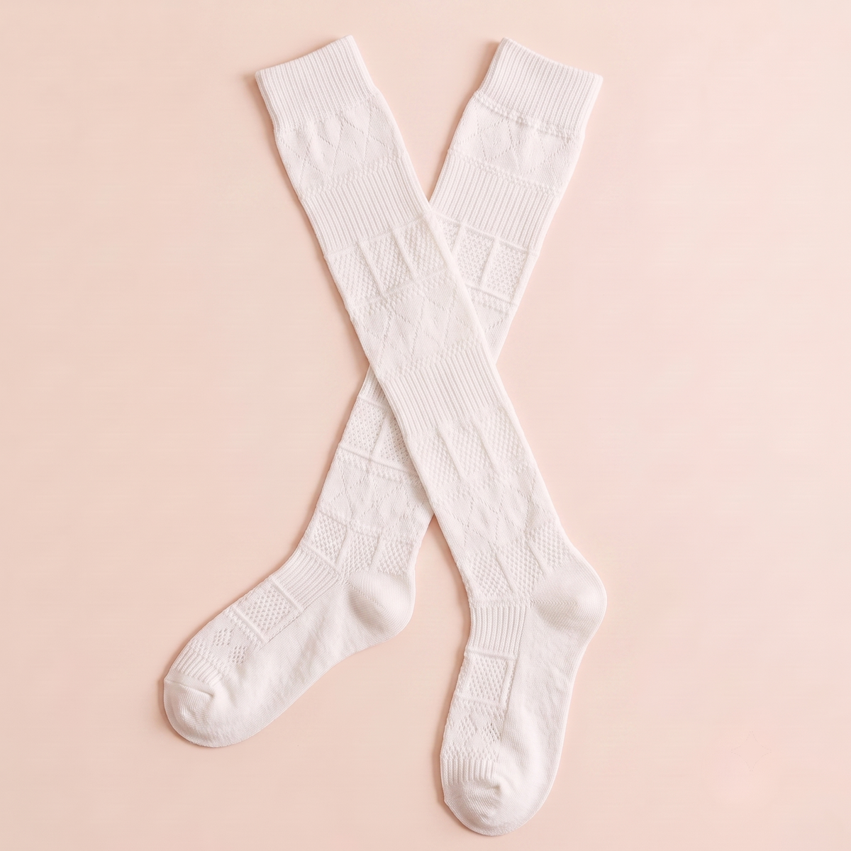 Mid calf boot socks in white pointelle knit, featuring a delicate openwork texture. Two socks crossed on a warm beige background.