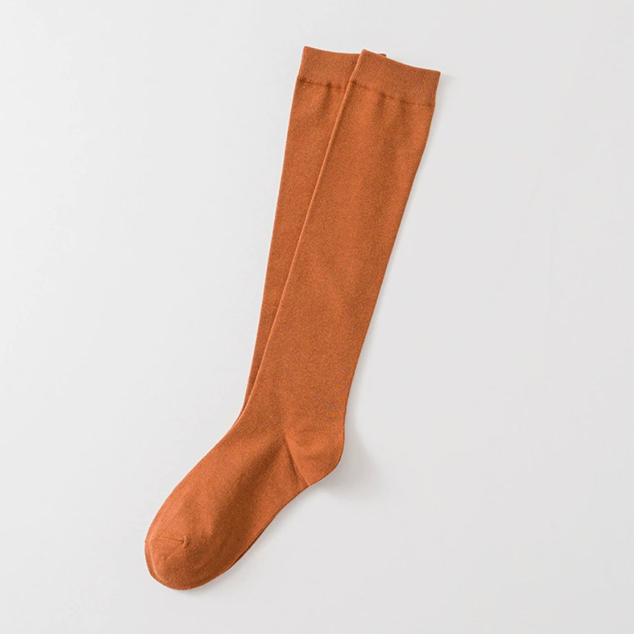 Orange knee high socks in warm orange ribbed knit, featuring a smooth knee-high leg. Shown as a single flat-lay on a neutral backdrop.