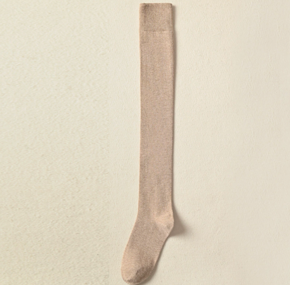 Over knee socks in beige ribbed knit, featuring a long thigh-high leg. Shown as a single flat-lay on a light backdrop.