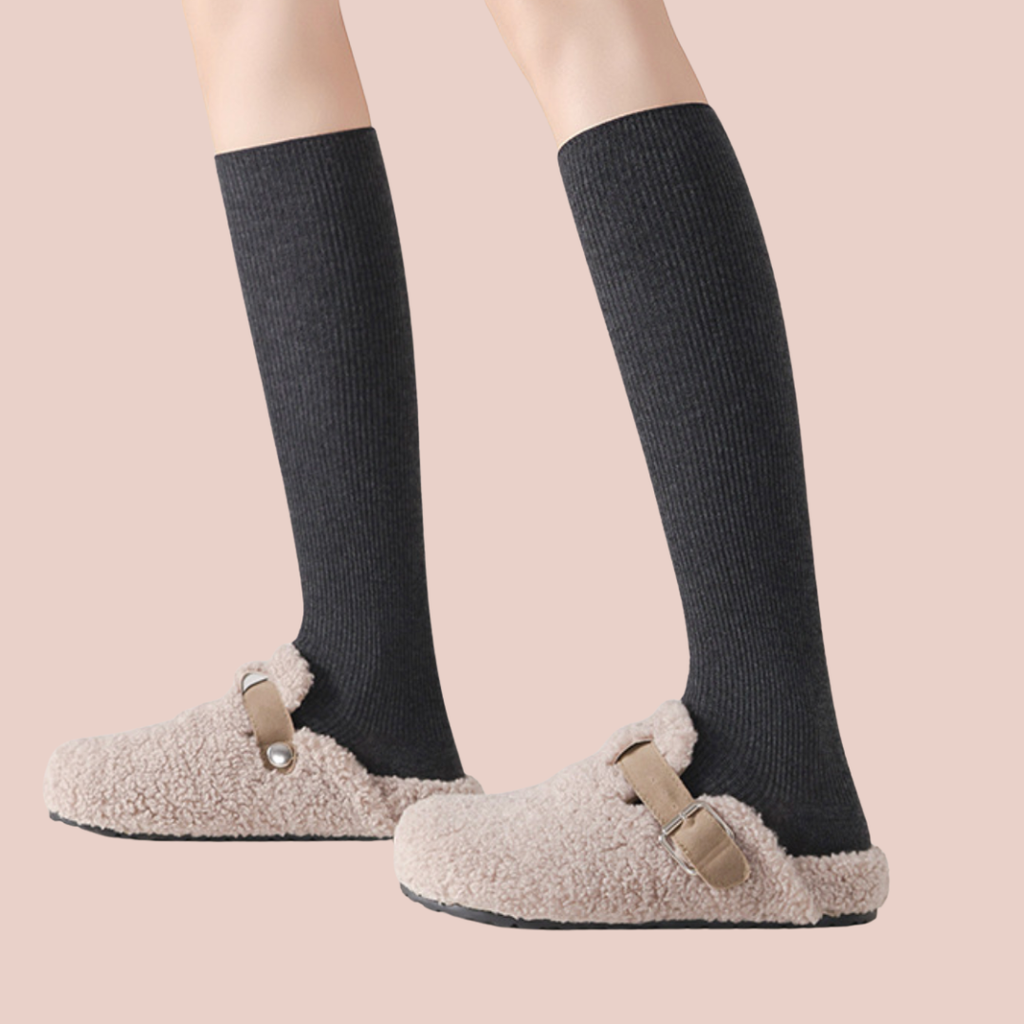 Over the calf wool dress socks in grey ribbed wool, featuring a long leg. Worn with fuzzy slippers.