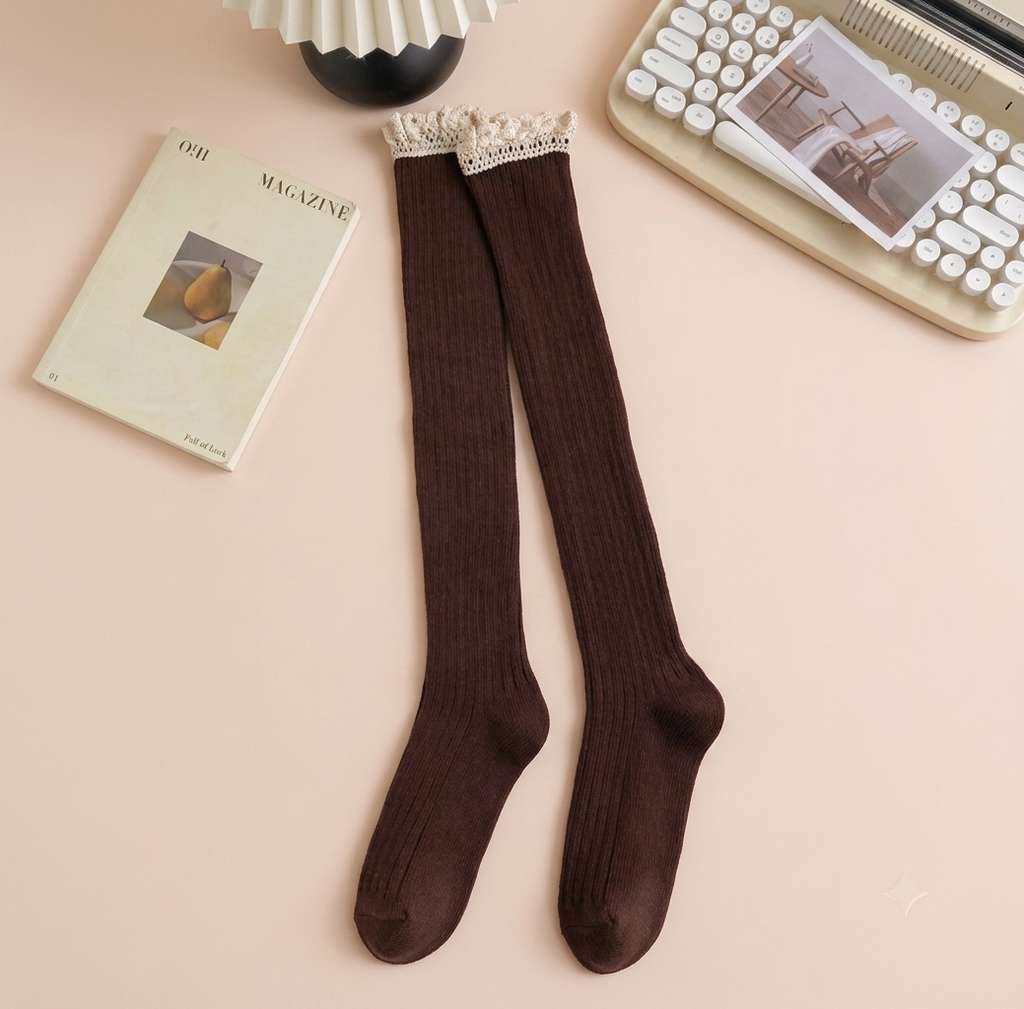 Over the knee boot socks in dark brown, featuring a ribbed thigh-high length. Styled flat beside a book and keyboard.